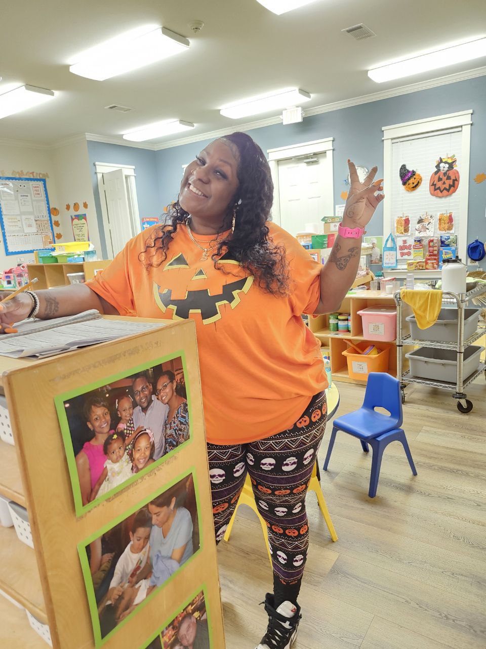 A smiling teacher wearing a pumpkin shirt and halloween leggings.
