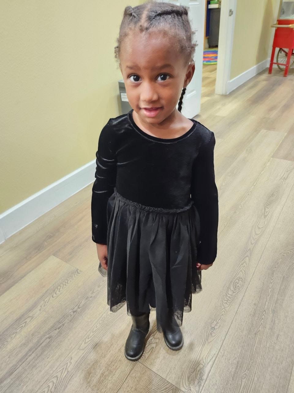 A girl in a black velvet dress with a tulle skirt and black boots standing in a hallway.