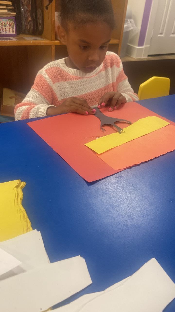 A girl cutting a strip of yellow paper with scissors during an art project.