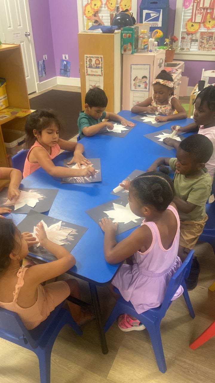 Children around a blue table making white paper crafts on black paper.