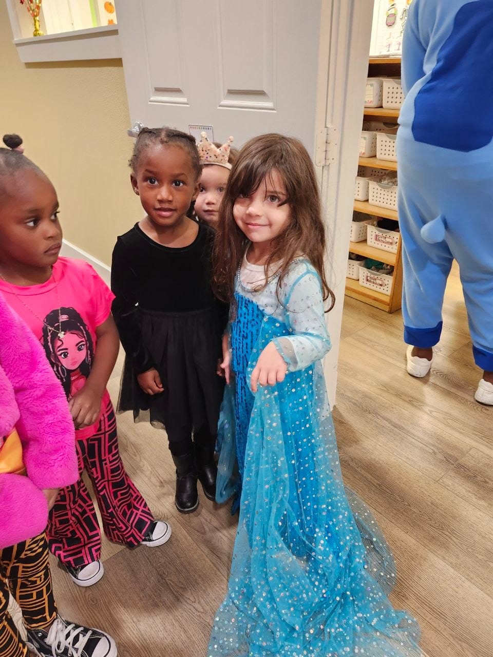 A group of dressed-up kids in a hallway, including a girl in a sparkly blue gown with a long sheer cape.