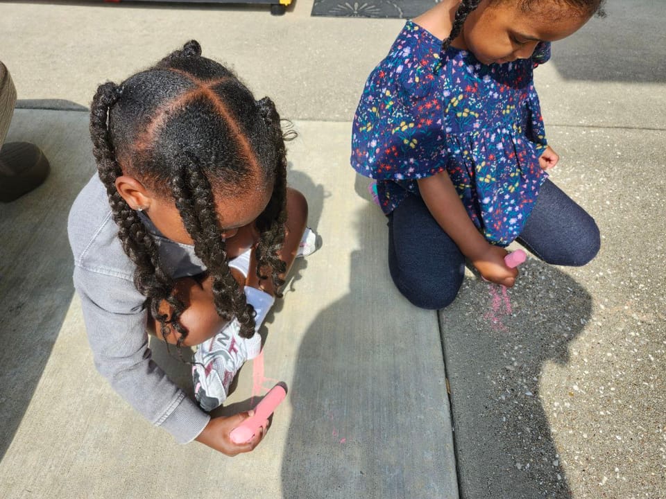 Two girls drawing with chalk on the sidewalk.