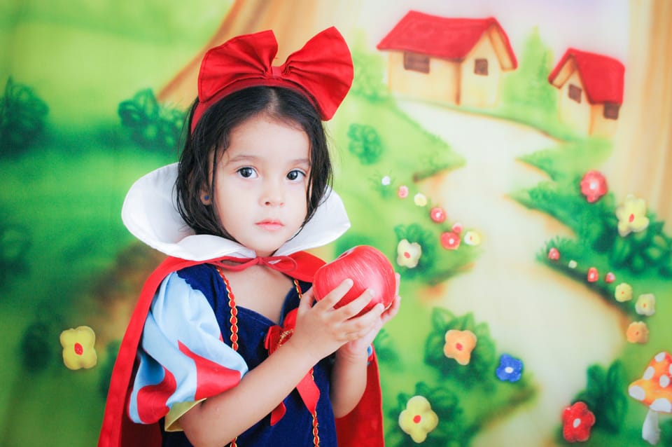 A young girl dressed as Snow White holding a red apple.
