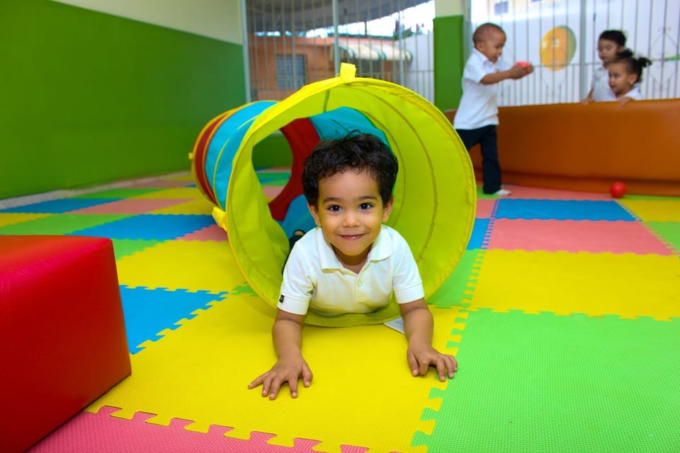 A crawling child smiling at the end of a play tunnel.