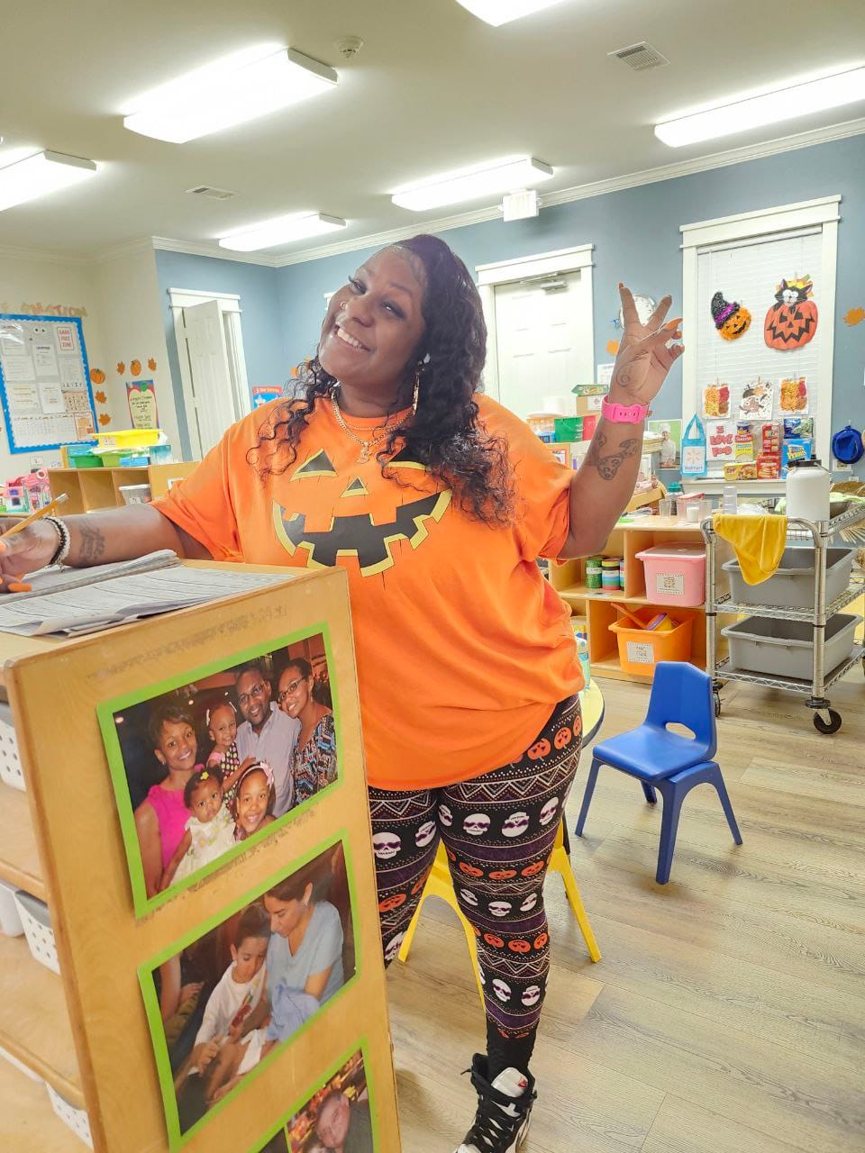 A smiling teacher wearing a pumpkin shirt and halloween leggings.